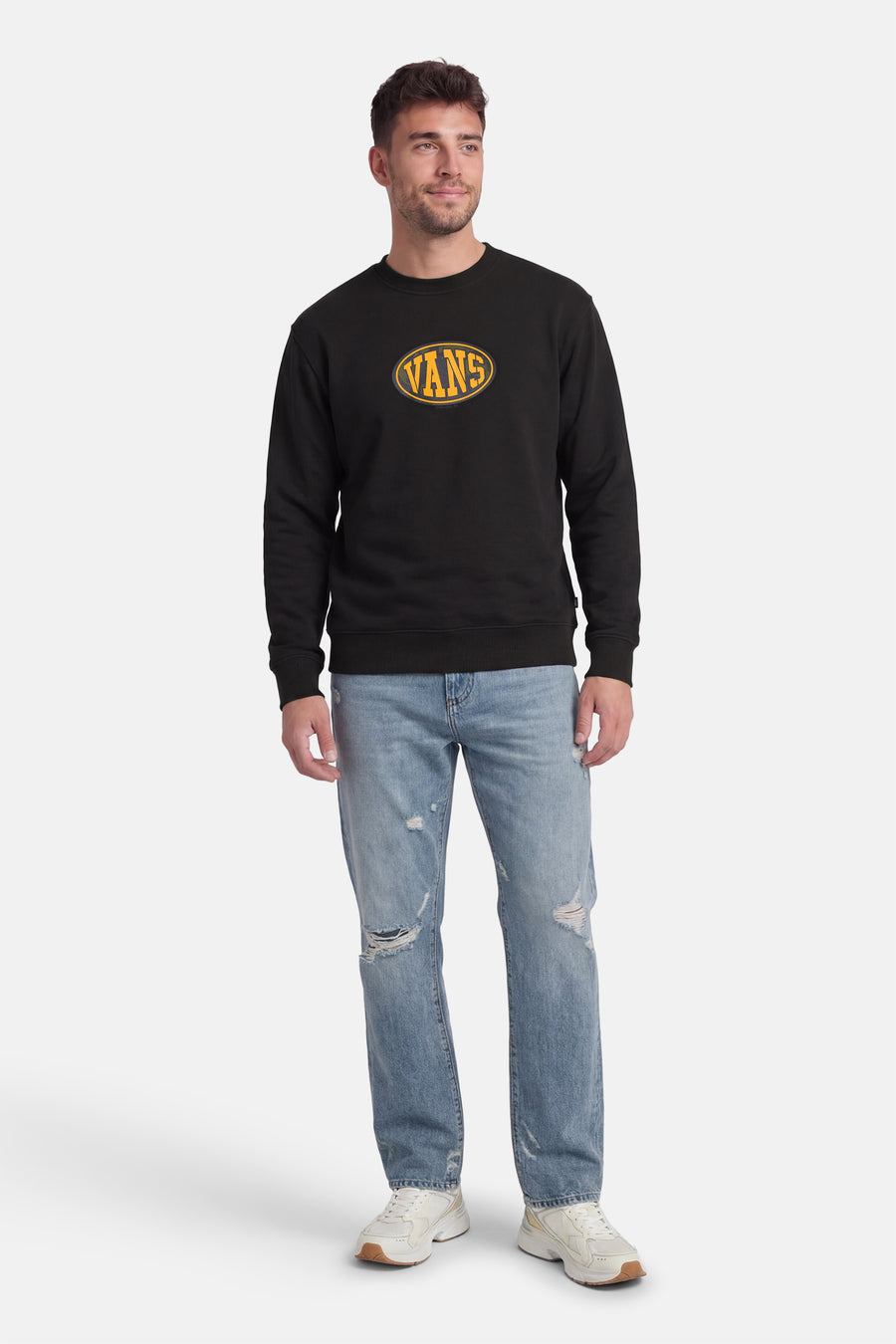Zwarte sweater van VANS “OFF THE WALL” met geel logo op de borst, gecombineerd met een blauwe jeans en witte sneakers.
