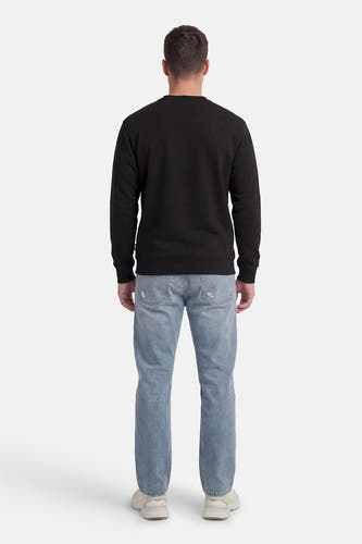 Zwarte sweater van VANS “OFF THE WALL”, met lange mouwen en ronde hals, gecombineerd met een spijkerbroek en sneakers, van achteren gezien.