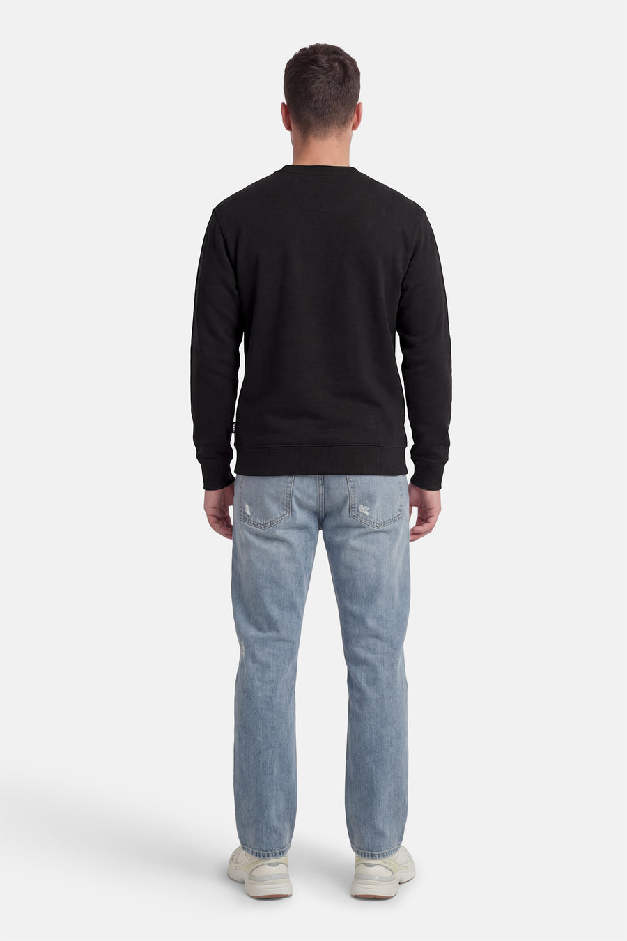 Zwarte sweater van VANS “OFF THE WALL”, met lange mouwen en ronde hals, gecombineerd met een spijkerbroek en sneakers, van achteren gezien.