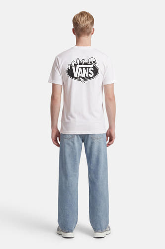 T-shirt blanc VANS avec imprimé tête de mort et main dans le dos, porté avec un jean bleu clair et des baskets grises.
