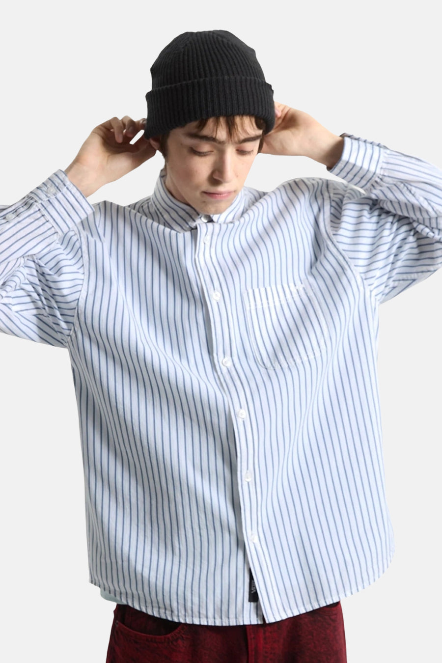 Chemise blanche à rayures VANS "OFF THE WALL", portée par une personne de dos, avec un bonnet noir et un pantalon bordeaux.