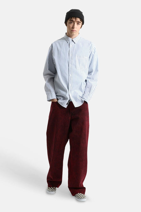 Chemise à manches longues rayée bleu et blanc de VANS "OFF THE WALL", coupe oversize, portée avec un bonnet noir, un pantalon rouge et des chaussures à enfiler à carreaux.