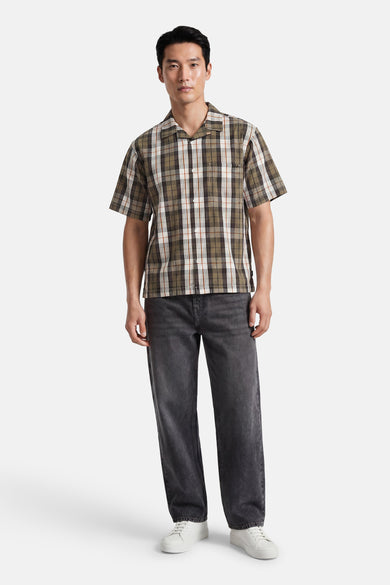 Chemise multicolore à manches courtes VANS "OFF THE WALL" à motif à carreaux vert, marron et blanc, associée à un jean foncé et des baskets blanches.