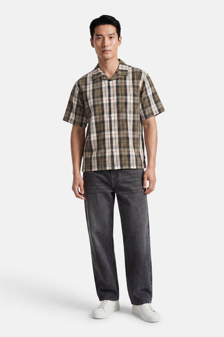 Chemise multicolore à manches courtes VANS "OFF THE WALL" à motif à carreaux vert, marron et blanc, associée à un jean foncé et des baskets blanches.