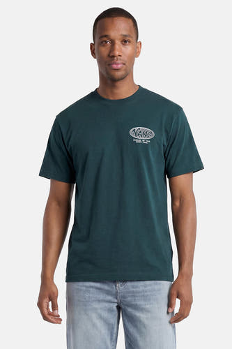 Donkergroen T-shirt van VANS “OFF THE WALL” met witte ovale wereldbolprint en VANS-logo op de borst, gedragen door een man met een lichtblauwe jeans.