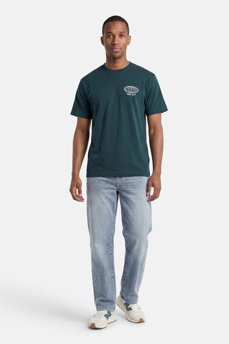 T-shirt vert de VANS avec un logo ovale blanc et le texte 'FOREVER ON TOUR SINCE 1966', porté par un homme avec un jean clair et des baskets beiges.