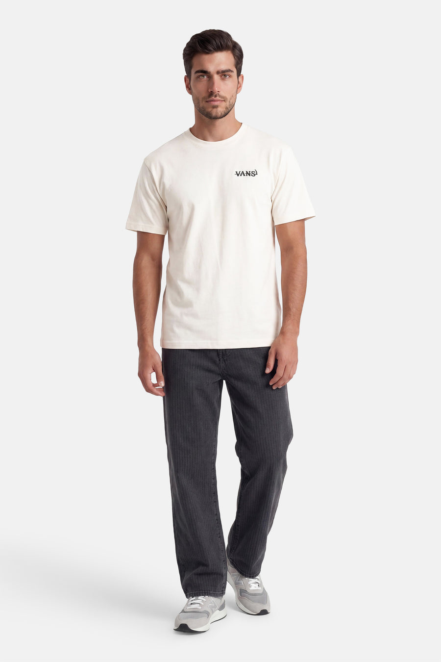 T-shirt écru à manches courtes VANS "OFF THE WALL" avec logo noir sur la poitrine, porté avec un pantalon côtelé gris foncé et des baskets grises.