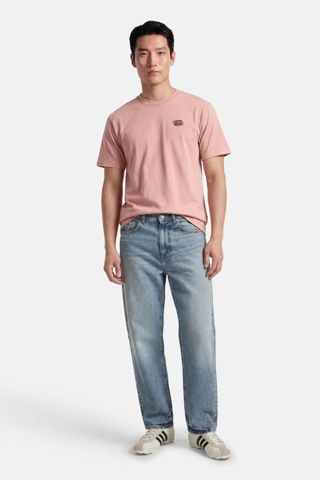 T-shirt rose VANS "OFF THE WALL", à manches courtes, porté avec un jean et des chaussures de couleur crème.