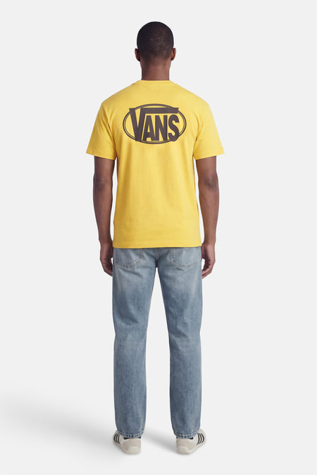 T-shirt jaune à manches courtes VANS "OFF THE WALL", avec un graphique ovale au dos, porté avec un jean et des baskets.