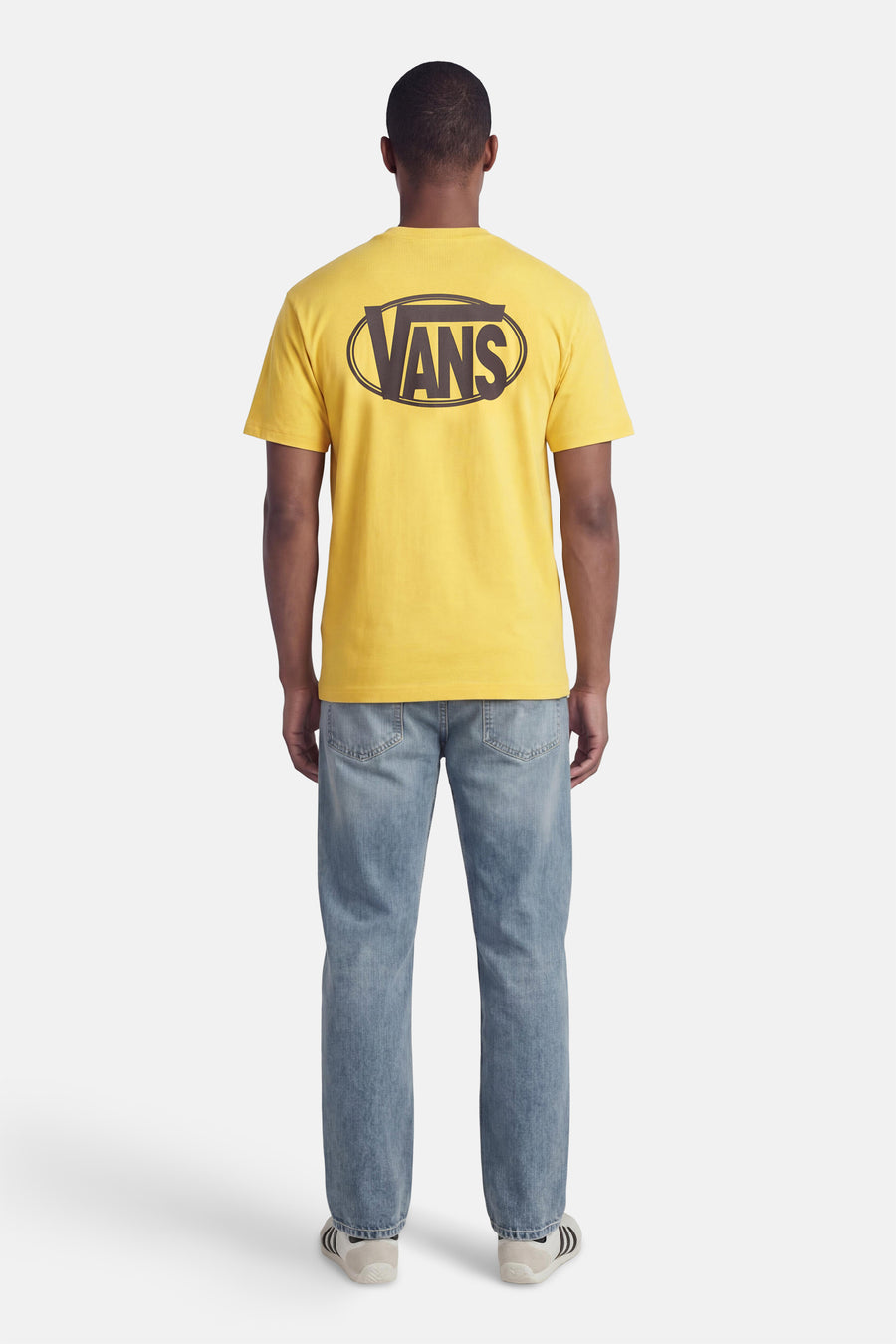 T-shirt jaune à manches courtes VANS "OFF THE WALL", avec un graphique ovale au dos, porté avec un jean et des baskets.