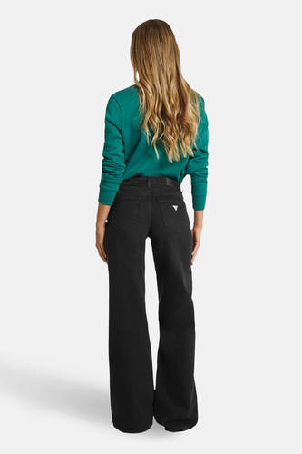 Jean décontracté noir de denim de Guess, avec une partie arrière visible, associé à un pull vert.