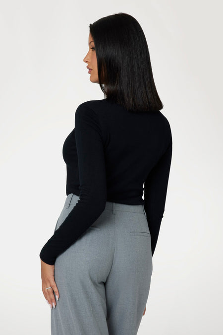 Zwarte pull met rolkraag van Guess®, met lange mouwen, gedragen door een model in grijze broek, zijaanzicht.