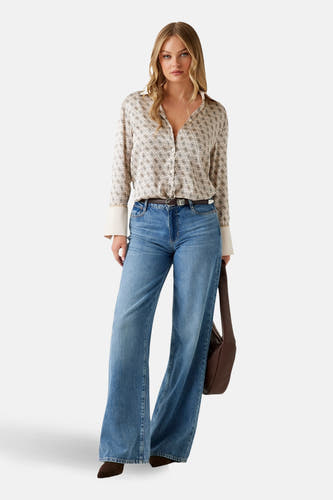 Chemise beige à longues manches de Guess, avec un imprimé et des poignets blancs, portée avec une ceinture brune et des jeans bleus.