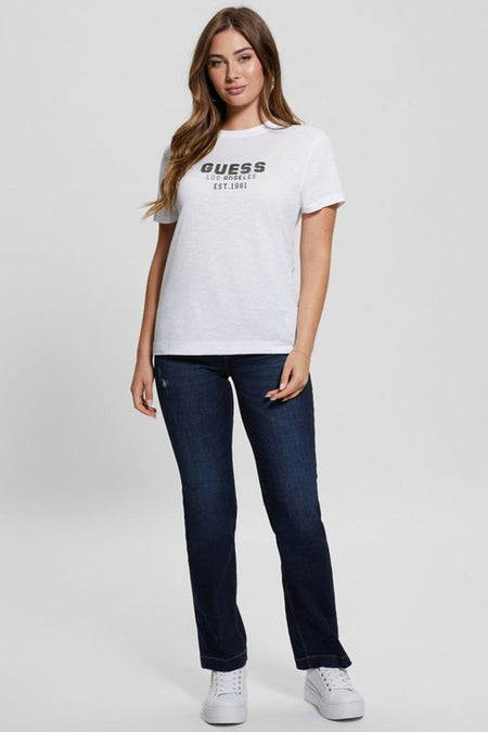 T-shirt blanc à manches courtes Guess avec imprimé noir 'Guess Los Angeles Est. 1981', combiné avec un jean bleu foncé et des baskets blanches.