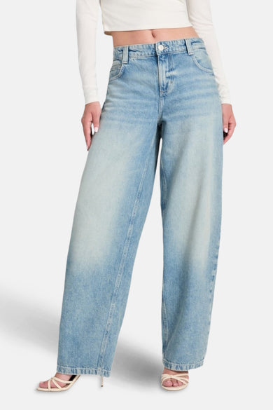 Jean en denim bleu clair à larges jambes de Guess, associé à une chemise blanche et des sandales.