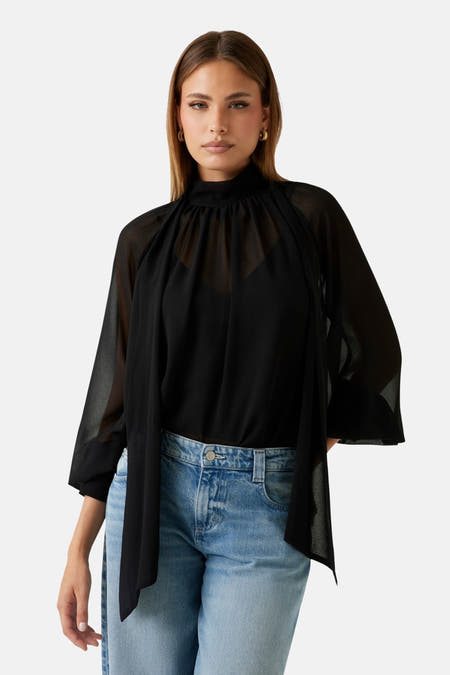 Blouse noire à manches longues de Guess, en tissu transparent et portée avec un jean bleu.