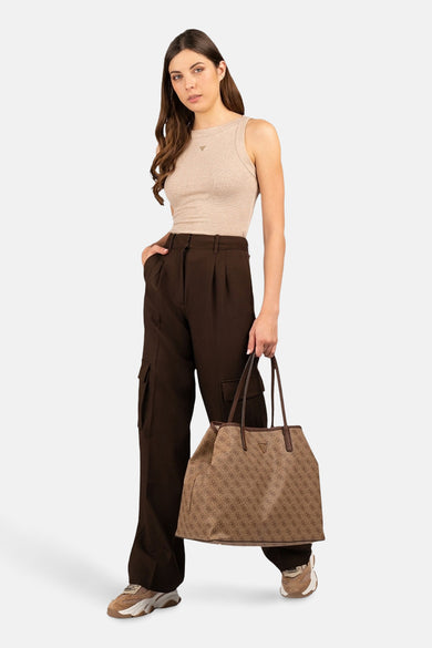 T-shirt beige sans manches de Guess, porté avec un pantalon marron et une poche main main avec imprimé logo.