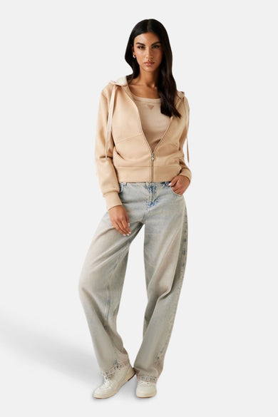 Pull-over marron avec capuche de Guess à fermeture éclair ouverte, associé à un tank-top et des jeans larges.