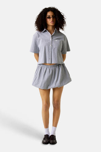 Chemise noire à manches courtes de Guess, à motif à carreaux, portée avec une jupe à volants et des chaussettes blanches.