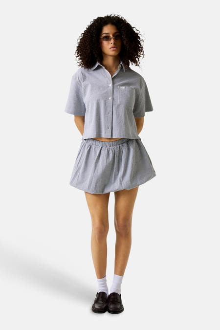Chemise noire à manches courtes de Guess, à motif à carreaux, portée avec une jupe à volants et des chaussettes blanches.
