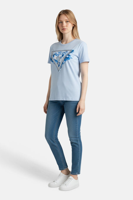 T-shirt bleu (manches courtes) de Guess®, avec un imprimé triangulaire et porté avec un jean et des baskets blanches.