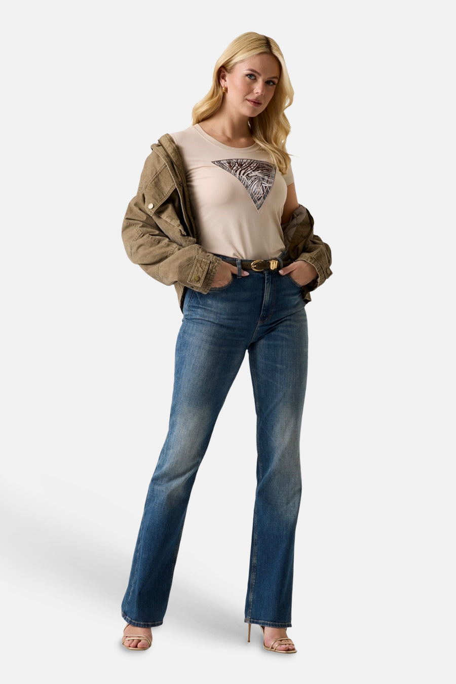 T-shirt beige à manches courtes de Guess, coupe ajustée avec une coupe courte, porté avec un jean bleu, vue de côté.