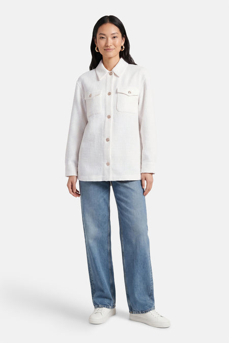 Wit hemd van Guess®, met lange mouwen en borstzakken, gecombineerd met een blauwe jeans en witte sneakers.