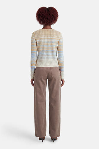 Gilet beige de Guess à manches longues, motif tricot rayé dans des tons clairs, vu de dos avec un pantalon large marron.