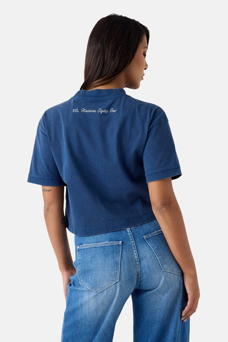 Blauwe korte mouw t-shirt van Guess® met witte tekst op rug, gedragen door model van achteren, gepaard met lichtblauwe jeans