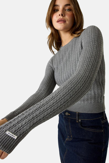 Grijze trui met ronde hals van Guess, met ribstructuur en label aan mouw, gedragen met donkerblauwe jeans, zijprofiel.