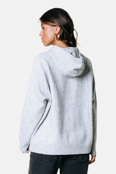 Sweat-shirt gris avec capuche de COLOURFUL REBEL, vu de dos, avec des boucles d'oreilles dorées et un short en jean.
