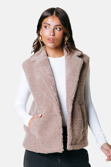Gilet bodywarmer beige de COLOURFUL REBEL, avec une douce texture teddy et un col revers, porté sur un t-shirt blanc.