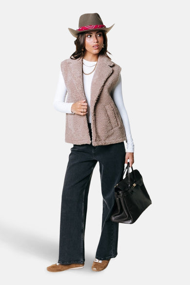 Gilet beige de COLOURFUL REBEL porté sur un t-shirt blanc à manches longues, associé à un pantalon noir et des chaussures marron, avec une sacoche noire.