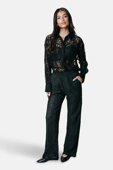 Pantalon noir de COLOURFUL REBEL, avec un motif en dentelle et une jambe droite, vu de derrière.