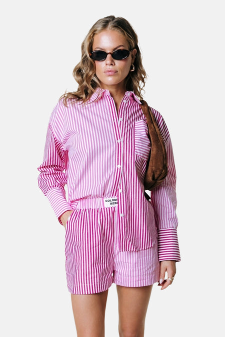 Short rose de COLOURFUL REBEL avec des rayures verticales blanches et une main dans la poche.