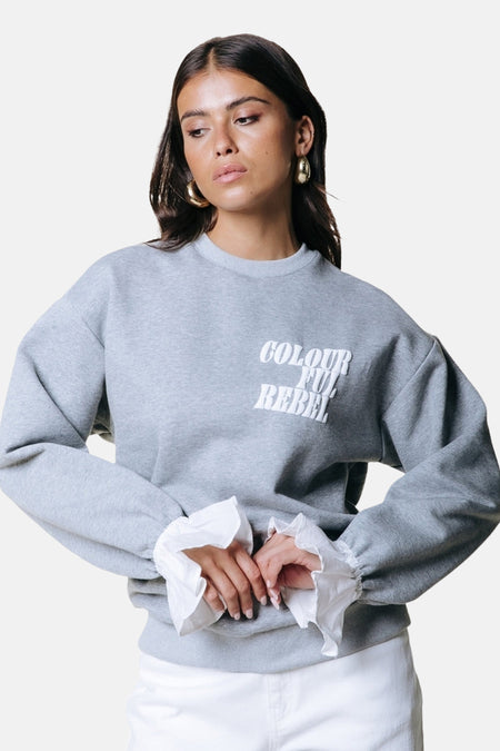 Pull gris de COLOURFUL REBEL avec des volants blancs aux manches.
