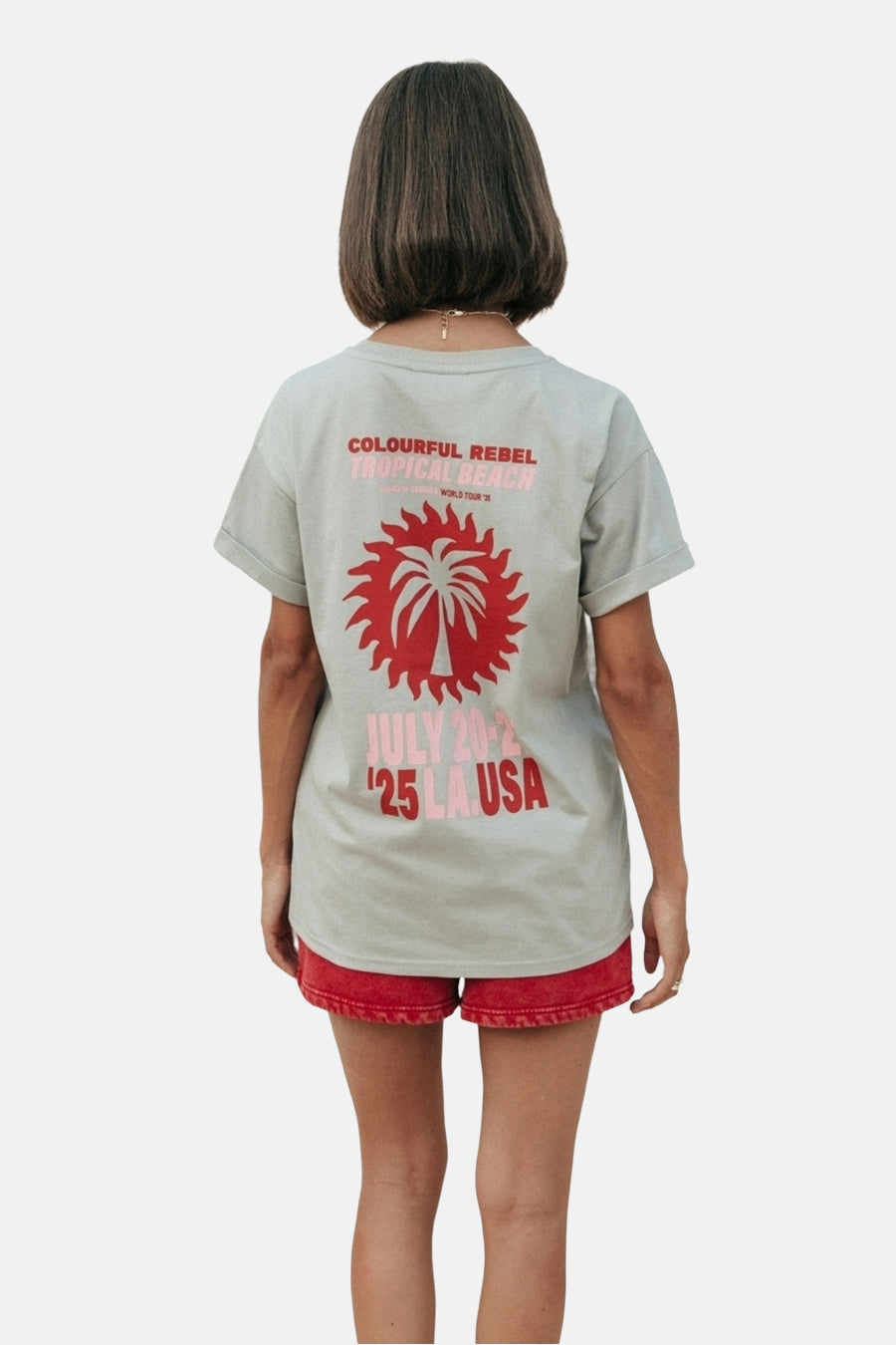 T-shirt gris à manches courtes de COLOURFUL REBEL, avec une imprimé tropique sur le dos, porté avec un short rouge.