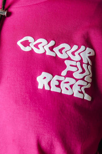 T-shirt rose de COLOURFUL REBEL avec texte blanc en relief 'COLOURFUL REBEL' sur la poitrine et un cordon de serrage noir partiellement visible.