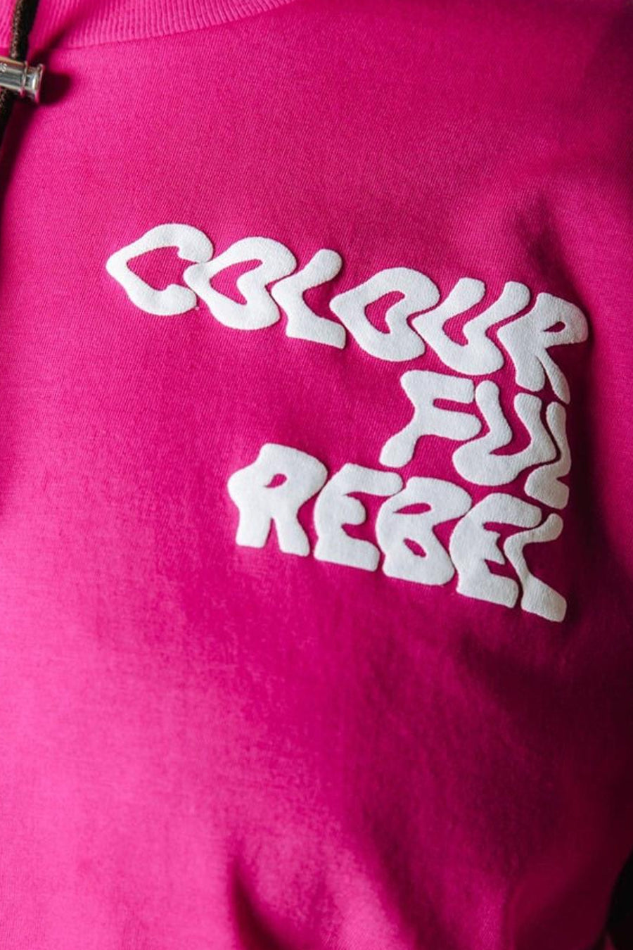T-shirt rose de COLOURFUL REBEL avec texte blanc en relief 'COLOURFUL REBEL' sur la poitrine et un cordon de serrage noir partiellement visible.