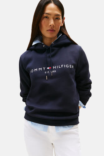 Pull à capuche bleu de TOMMY HILFIGER, avec lettres et détails blancs, combiné avec une chemise bleu clair et un pantalon blanc.