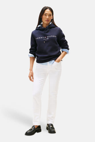 Blauwe sweater met kap van TOMMY HILFIGER, met witte letters en details, gecombineerd met een lichtblauw overhemd en witte broek.