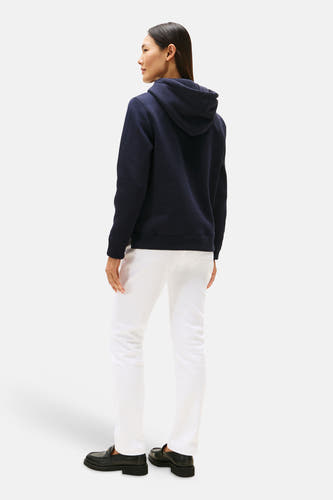 Pull à capuche bleu de TOMMY HILFIGER, vu de dos, avec un pantalon blanc et des chaussures noires.