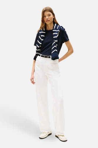 T-shirt bleu à manches courtes de Tommy Hilfiger, avec un pull rayé sur les épaules et un short blanc.