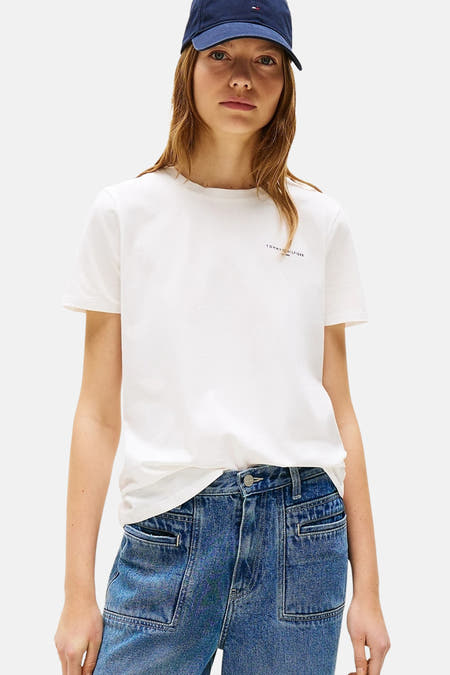 T-shirt blanc à manches courtes de TOMMY HILFIGER, associé à un chapeau de baseball bleu et des jeans avec poches.