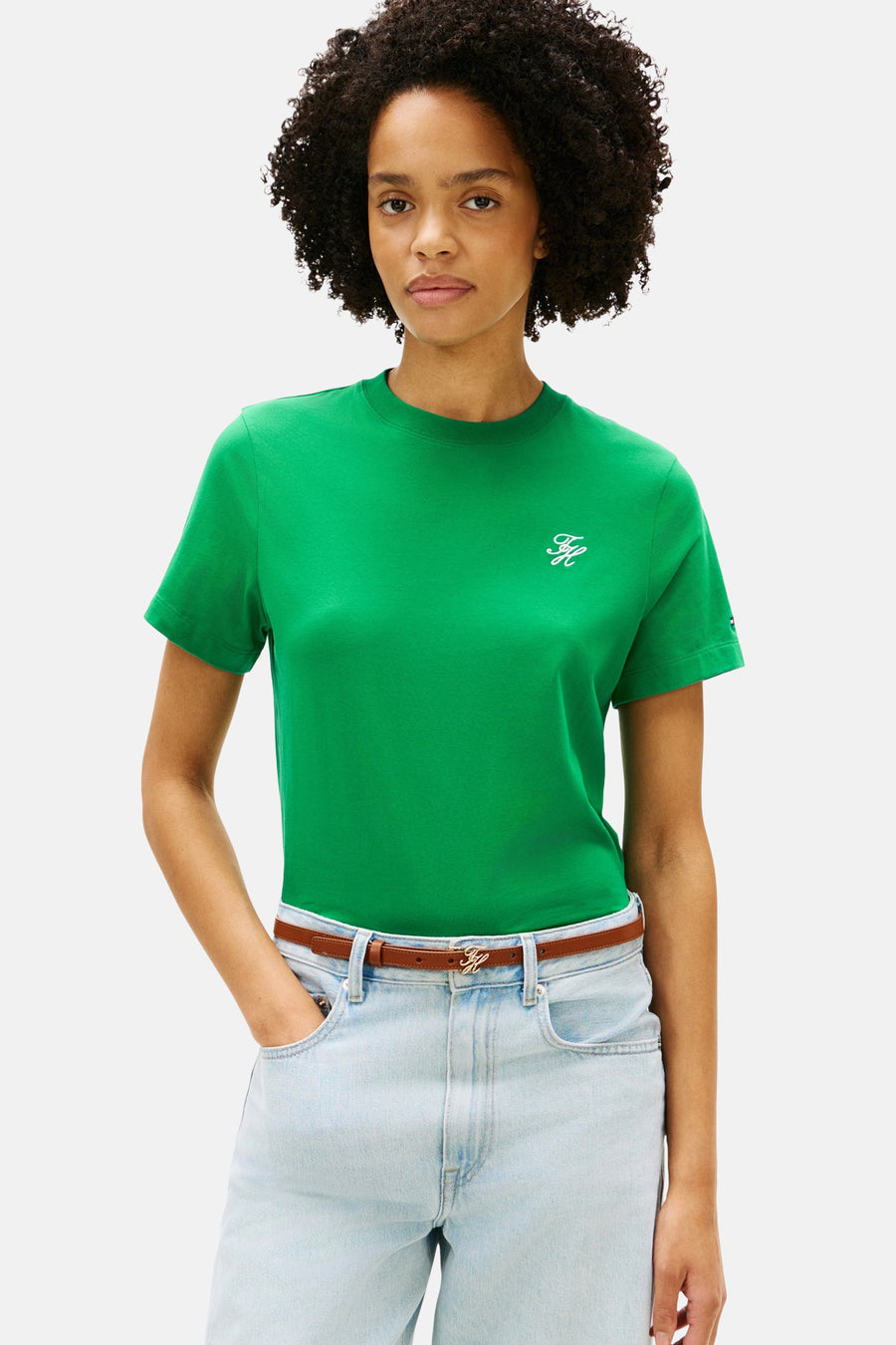 T-shirt vert Tommy Jeans de couleur verte, avec un petit logo, combiné avec une ceinture marron et un jean ample bleu clair.