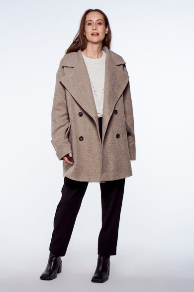 Manteau long gris de YŪGEN, avec une fermeture à double bouton, porté sur un pull en crème avec un pantalon noir et des bottines.