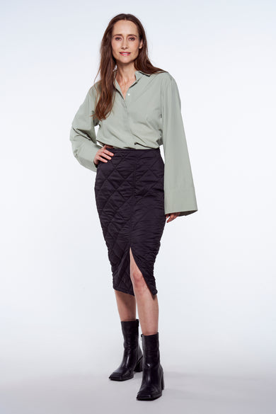 Chemise verte de YŪGEN, à manches longues et poignets, portée avec une jupe noire et des bottes.