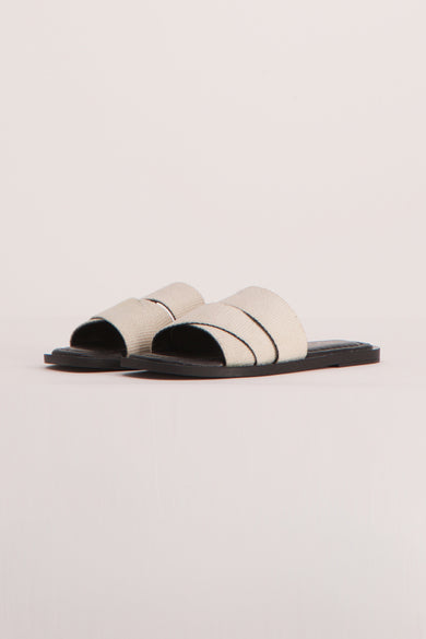 Sandales beige de YŪGEN, avec des brides croisées sur le pied et une semelle plate noire.