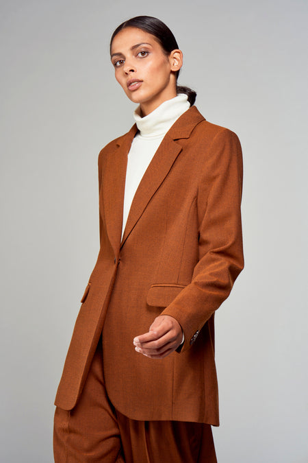 Blazer marron de YŪGEN porté sur une chemise blanche, avec un motif uni et une texture lisse.