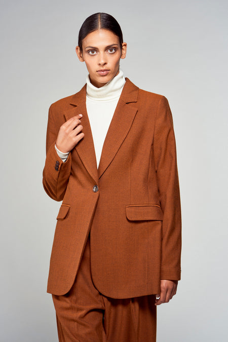 Blazer marron de YŪGEN, porté sur une chemise blanche, avec un seul bouton et des poches passepoilées.